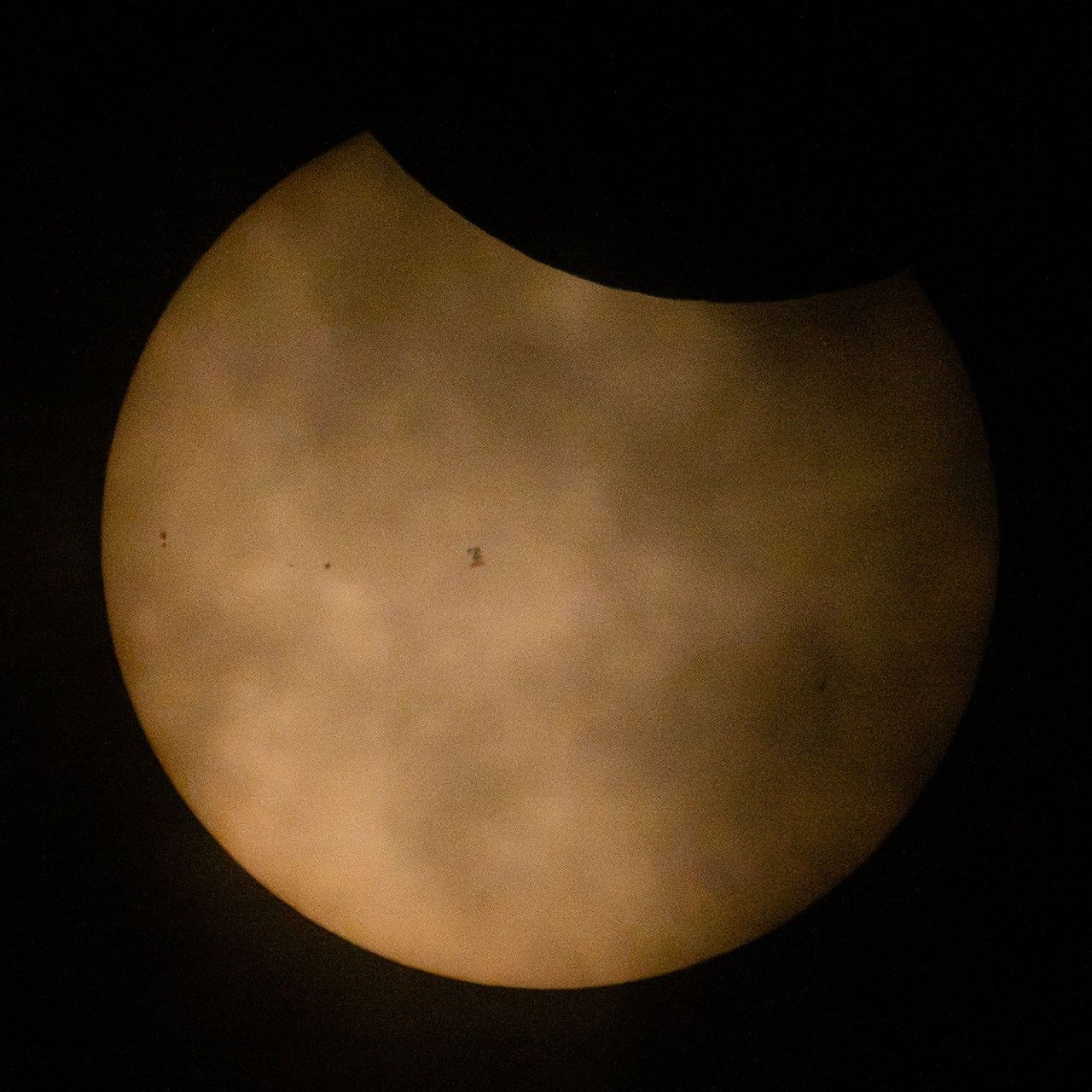 Silhouette of International Space Station against partially-eclipsed Sun.