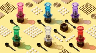 Collection of different colored AeroPress coffee makers lined up in a geometric formation with coffee beans, scoops, and sugar cubes