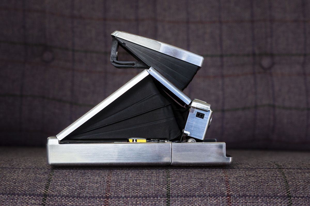 Polaroid SX70 camera side view and open in shooting position on purple chair