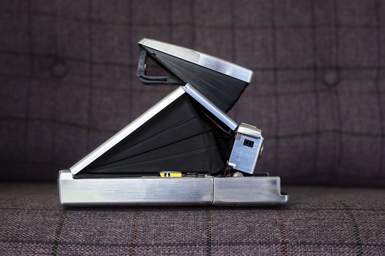 Polaroid SX70 camera side view and open in shooting position on purple chair
