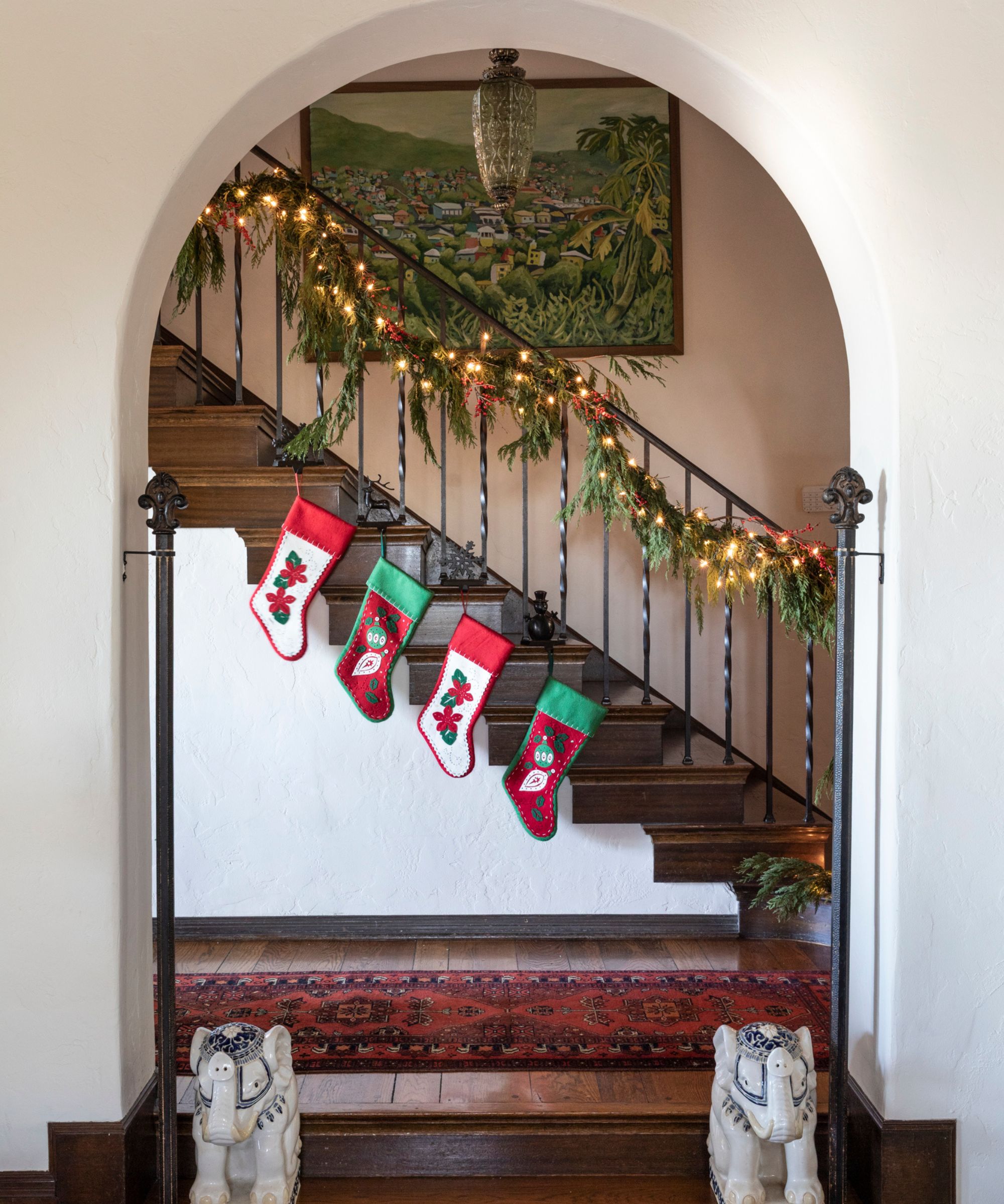 A white stairway with a natural garland draped over the banister and 4 stockings hung from the base