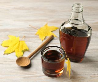Maple syrup in a pot and container on a table surrounded by yellow lwaves