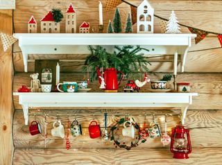 Two white shelves with various Christmas decorations on including bottle brush trees, white Christmas trees, red mugs, and more.
