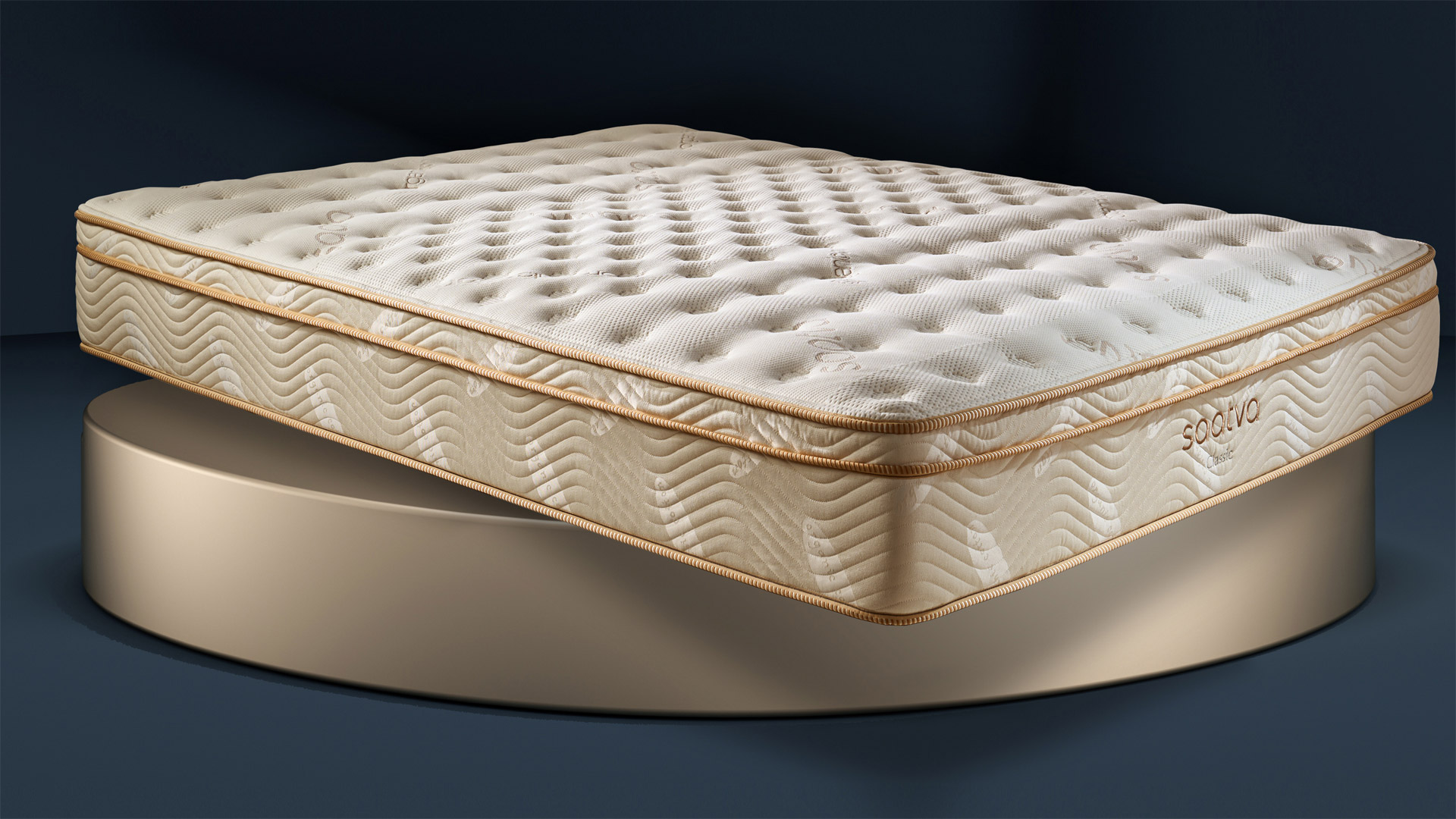 The Saatva Classic mattress photographed in our Sleep Lab during the review process, with the image showing it displayed against a blue-black background and placed on a large round gold plinth to match the golden piping along the edges of the mattress