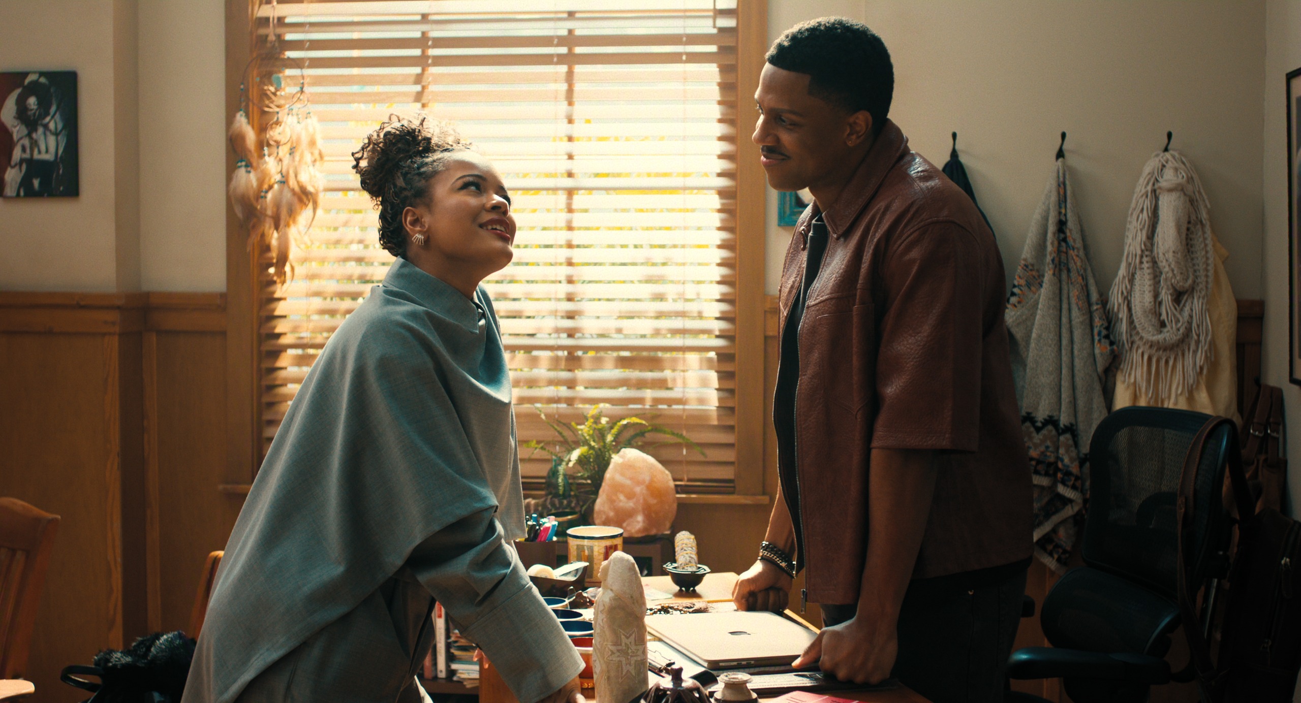Maleah Joi Moon as Deborah wearing a grey shall leaning over a desk in an office while talking to Vincent Jamal Hooper as Ellington in Episode 101 of Netflix's 'A Different World.'
