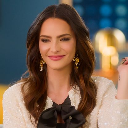 sandra vergara snaps her fingers wearing a white blouse with a black bow in a still from selling sunset