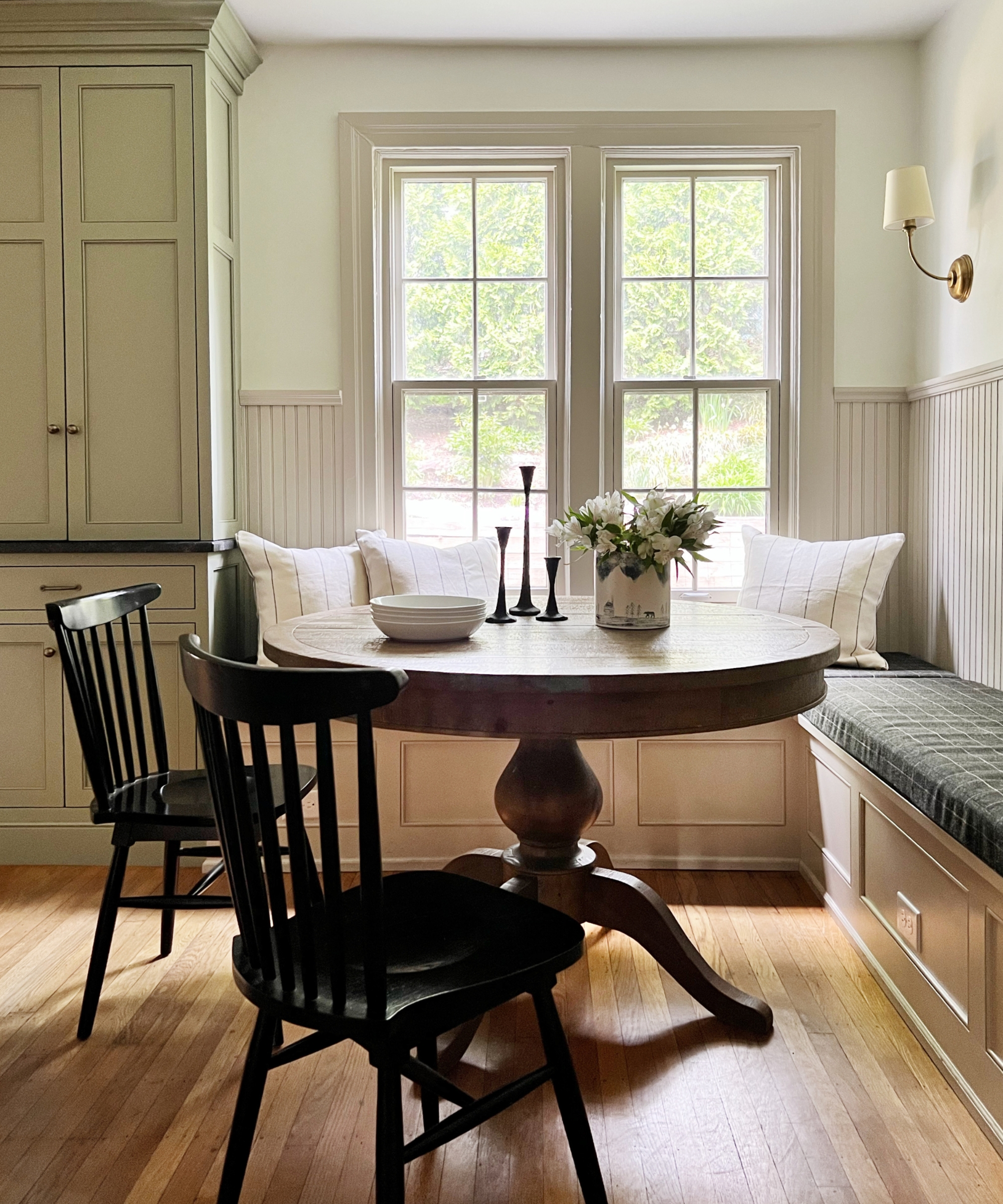 A kitchen nook with a dark wood round table, white walls, and cabinets painted in Revere Pewter by Benjamin Moore