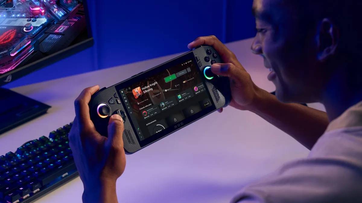 Asus ROG Xbox Ally X being played by person with monitor and keyboard on desk in background with over-the-shoulder angle
