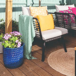 A patio with garden chairs and colourful cushions and a large blue flower pot