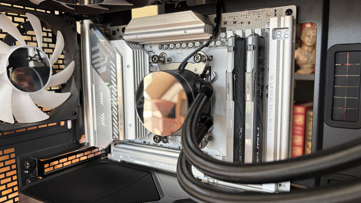 An MG-1 MK.II computer interior showing a motherboard with a silver heatsink, liquid cooling system, and visible RAM sticks. A cooling fan is on the left.