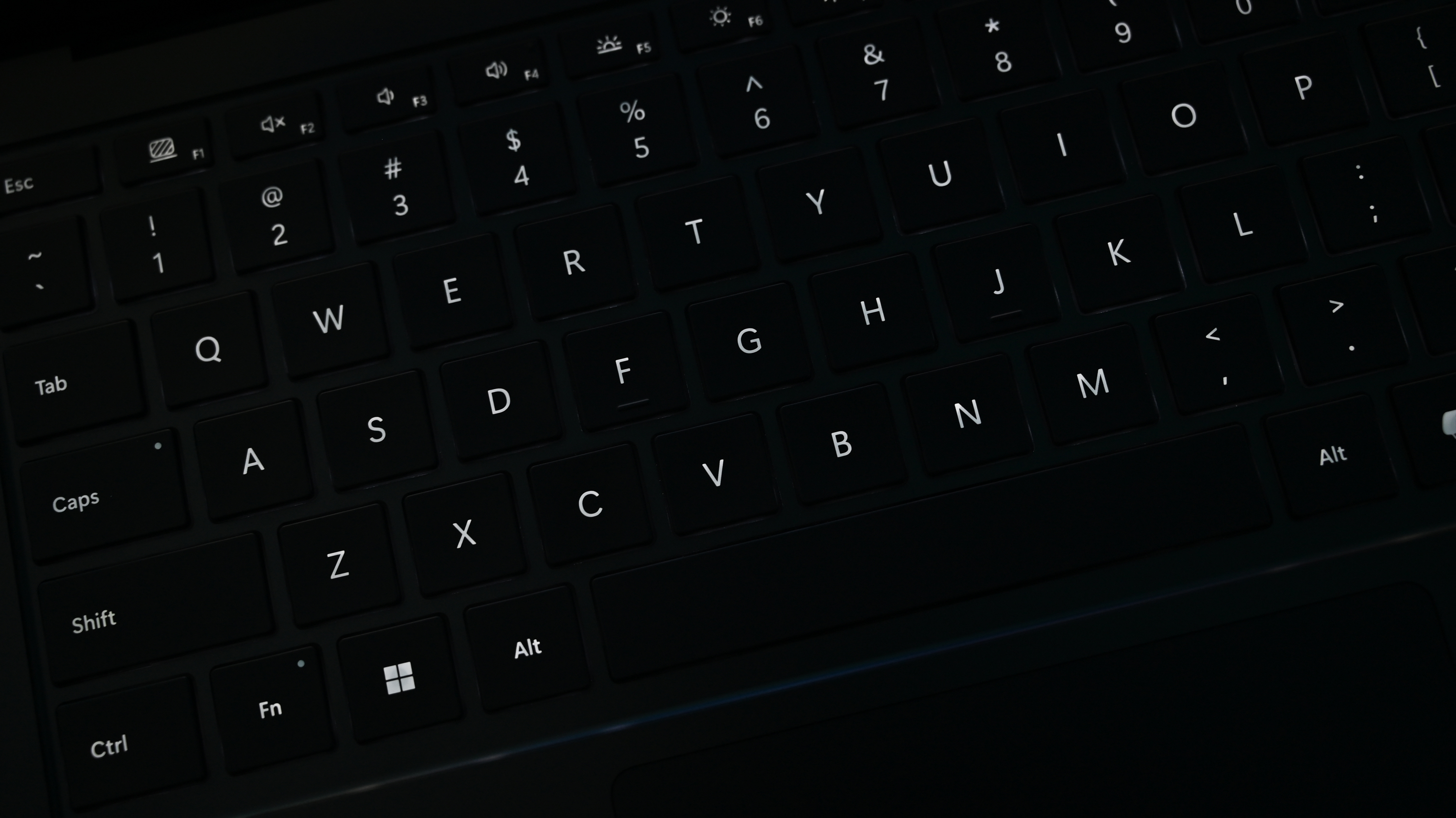Close-up of a dimly lit QWERTY keyboard with black keys. The letters and symbols are visible, creating a moody and focused atmosphere.