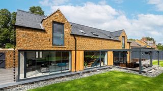 Stone-clad contemporary new build with large sliding doors, surrounded by a landscaped lawn and covered patio