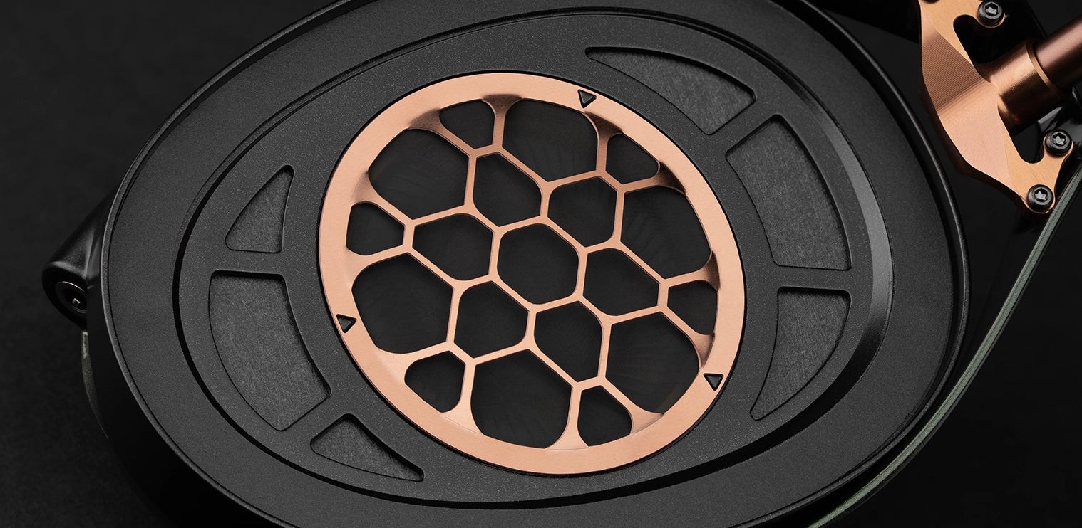 Toma macro detallada de la rejilla tipo panal de color cobre y el marco mecanizado con precisión dentro de los auriculares Meze Strada.