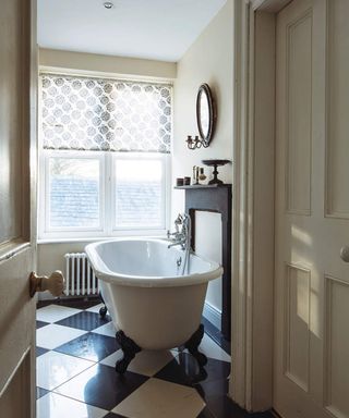 A cream bathroom with small white bathtub and black and white checkered tile flooring
