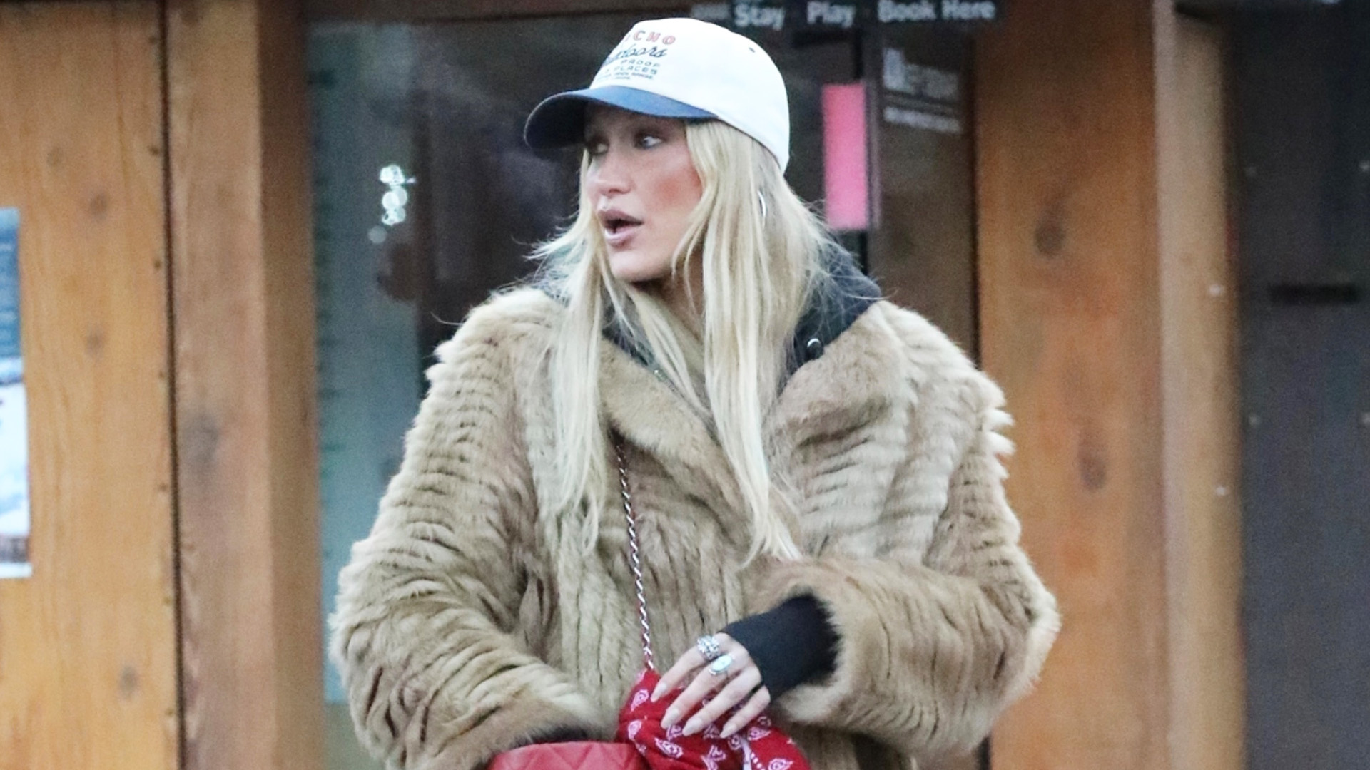 Bella Hadid wearing a fur coat, baseball cap, red triangle scarf, leggings, and Ugg Classic Tall Boots in Aspen