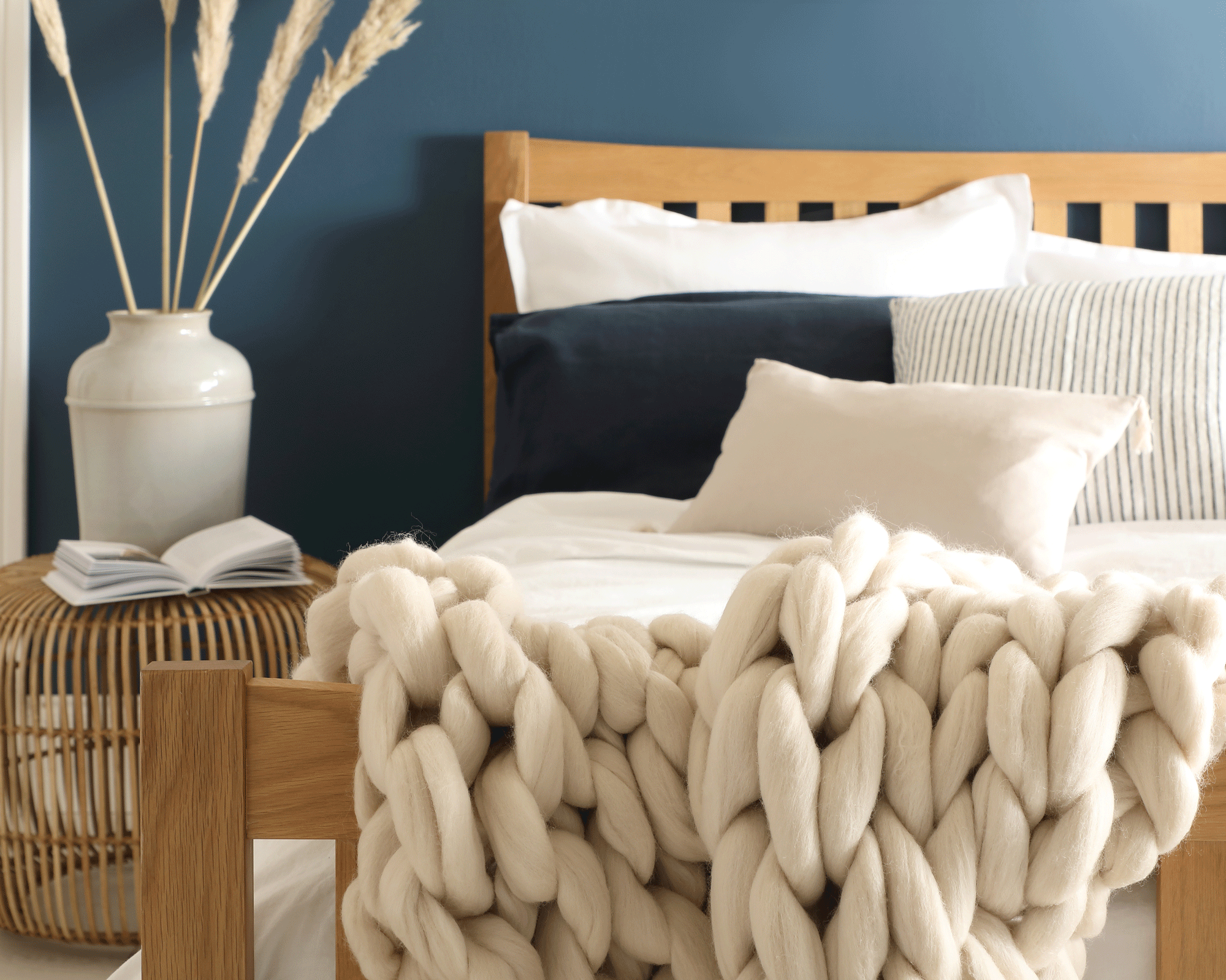 blue wall in bedroom with a luxurious bed and chunky knit throw