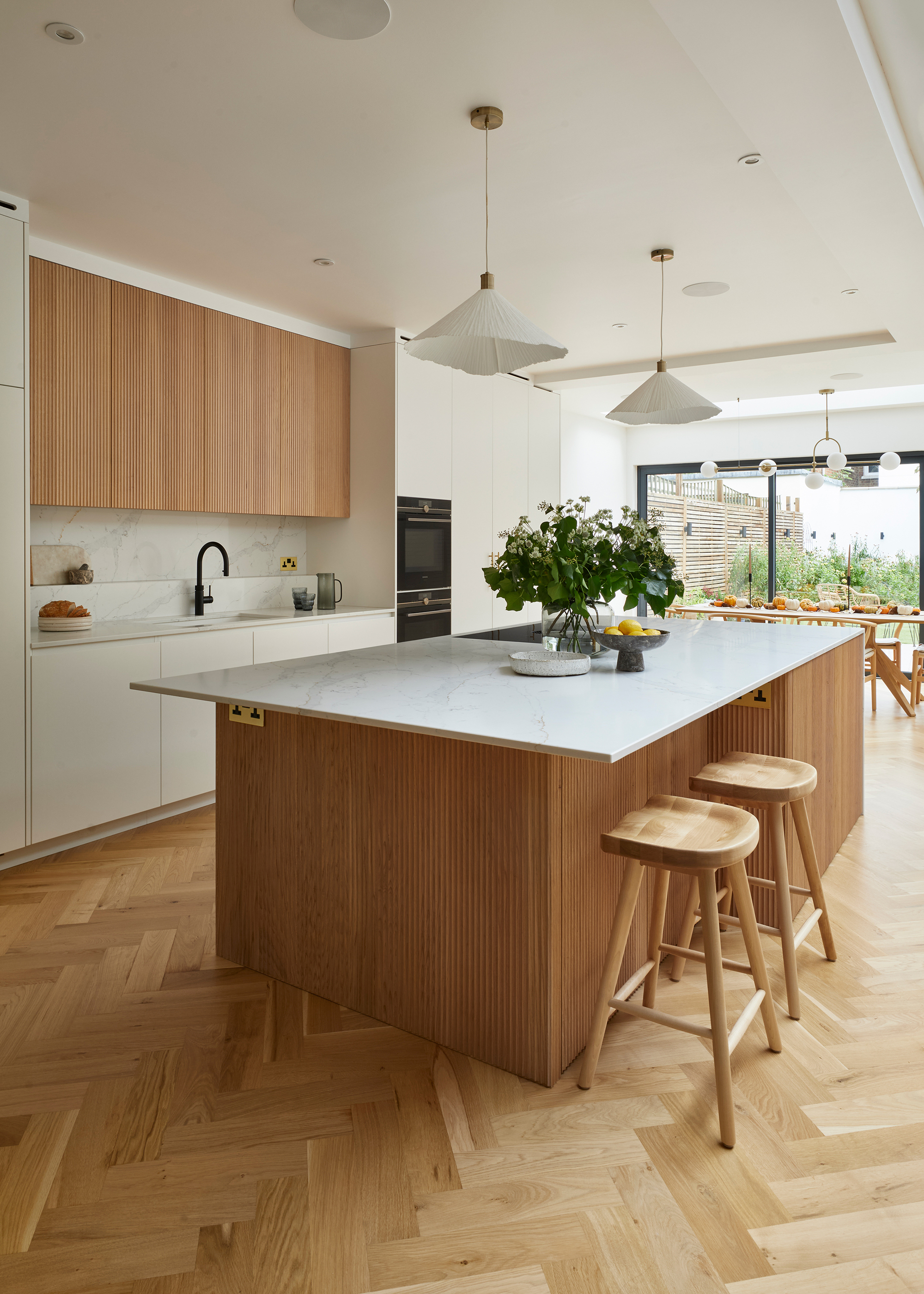 A kitchen with a wooden island, wooden upper cabinets, herringbone flooring, and white quartz countertop