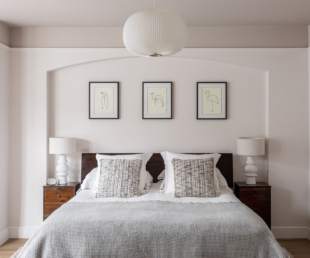 A double bed with cushions and a grey throw. There is a display of three framed prints above the bed