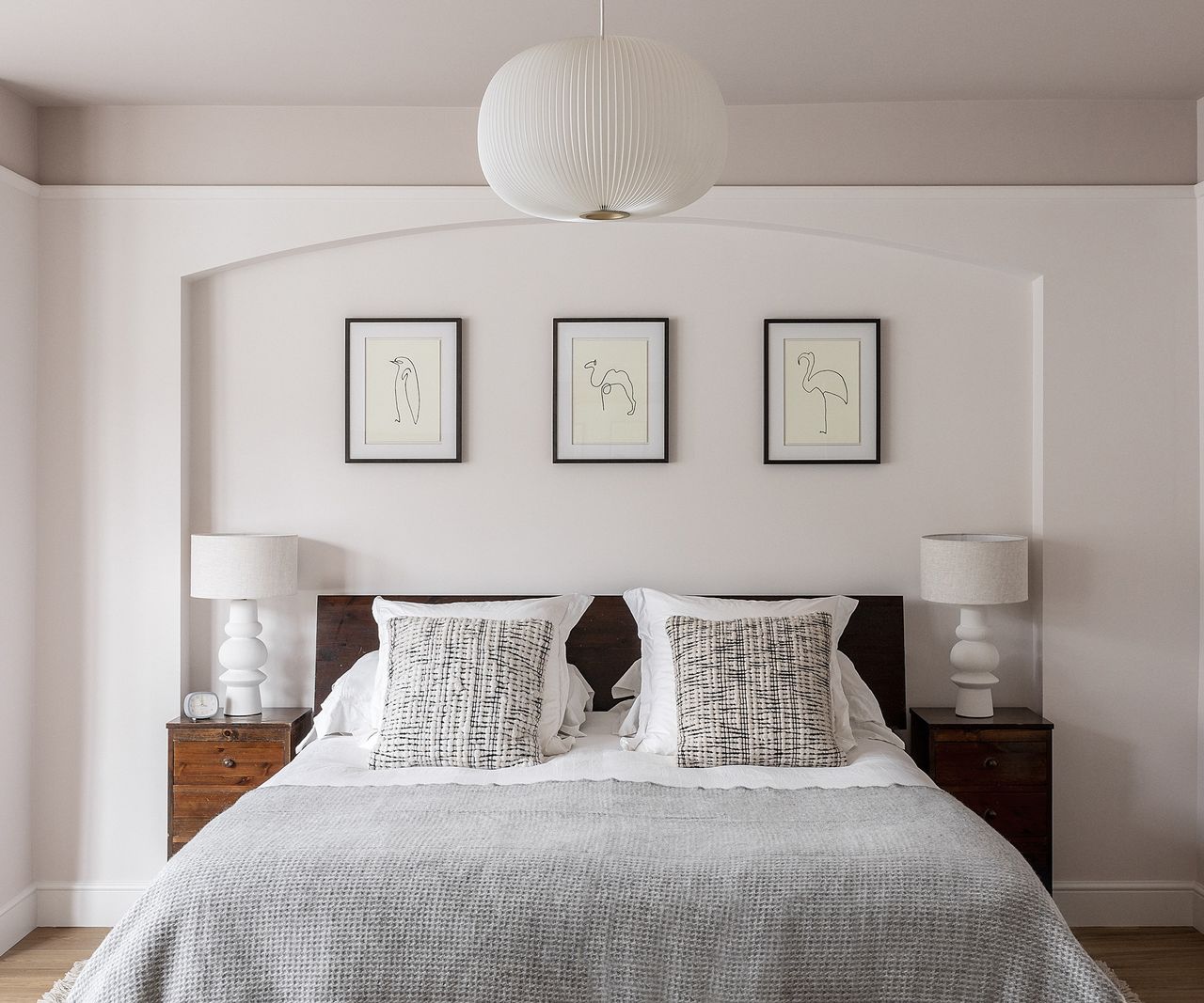 A double bed with cushions and a grey throw. There is a display of three framed prints above the bed
