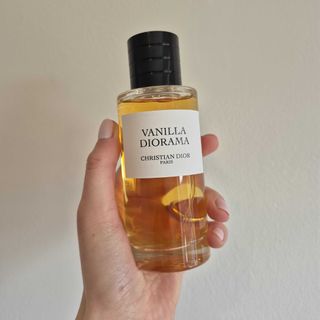 A close-up of Digital Beauty Writer, Naomi Jamieson's hand holding up Dior's Vanilla Diorama perfume against a cream wall