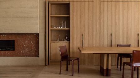 A minimalist dining room with wood cupboards a long wood table, shiny leather seating, and a stone fireplace