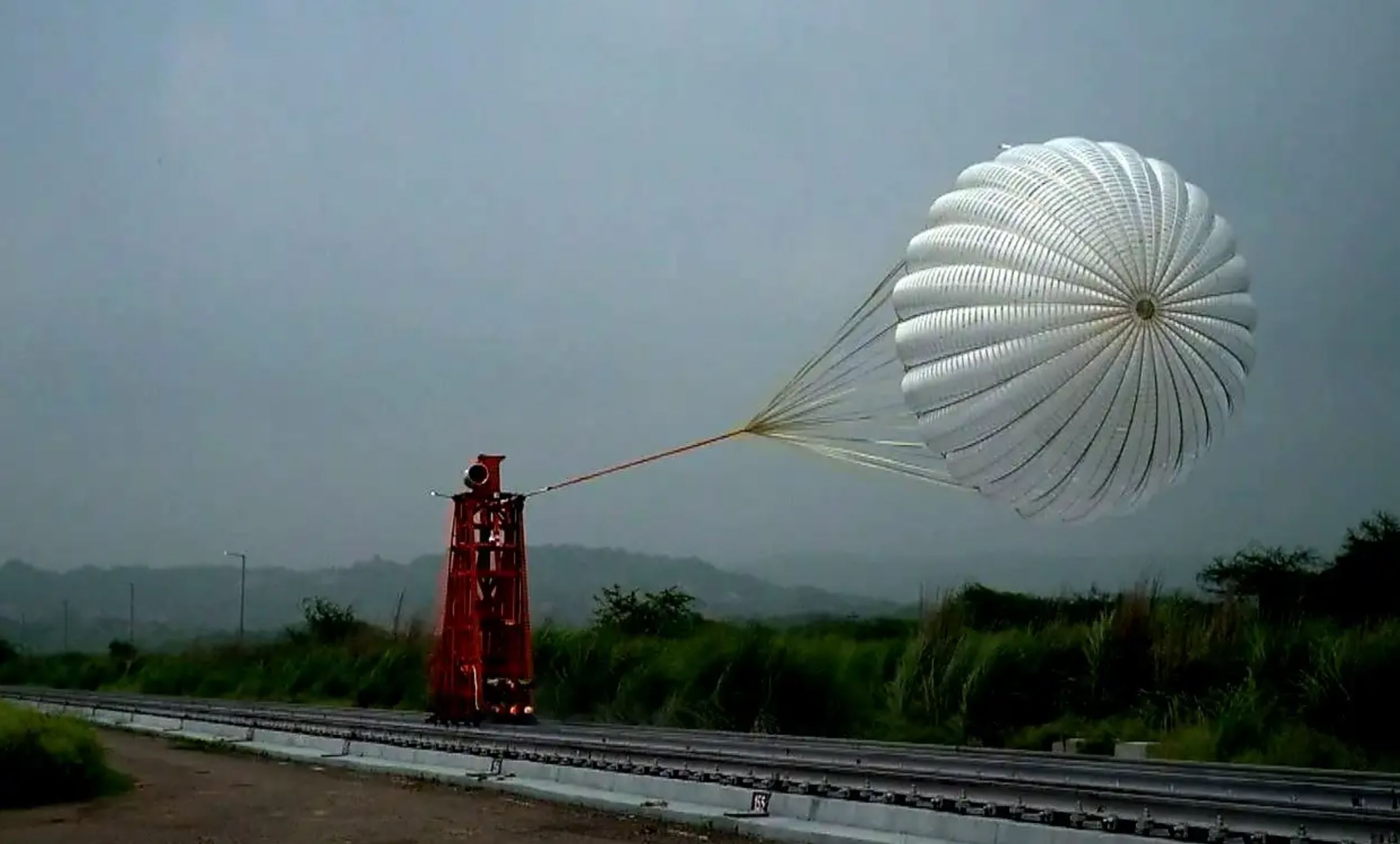 a metal stand is rocketed down train tracks as a parachute is pulled behind.