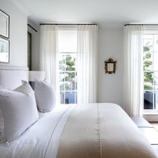 A bedroom with white bedding and two floor length windows