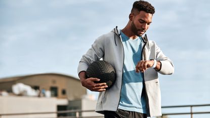 How to choose the right Fitbit for you: Pictured here, a person looking at a Fitbit on his wrist while holding a slam ball outdoors