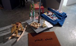 A floor area with a wooden rocking horse, a brown mat with Arabic text on it, various wooden toys and a square table with a tea set on it.