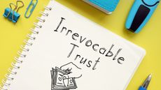 The words irrevocable trust written on a spiral notebook against a yellow background.