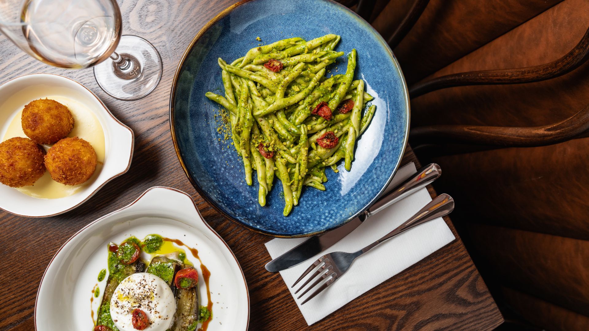 an image of a pesto pasta dish with a mozzarella side dish, and arancini side dish on top of a wooden table