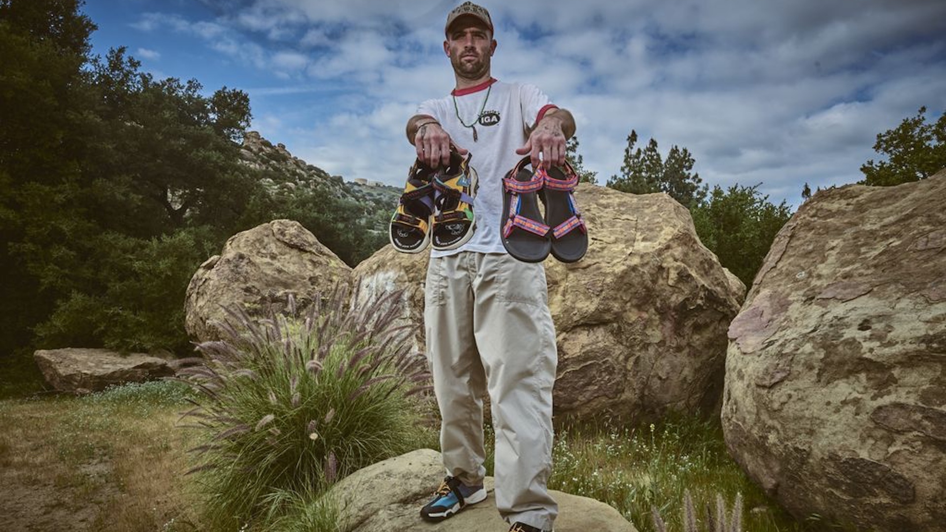 Sean Wotherspoon holding two pairs of sandals in the mountains from the Teva drop 