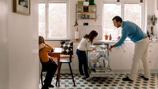 Father and daughter arranging utensils in dishwasher while standing at kitchen