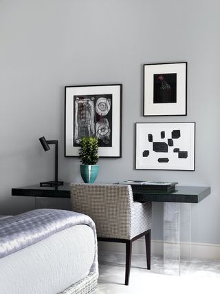gray bedroom with home office area, black desk, check chair, small gallery wall, desk light, bed in foreground