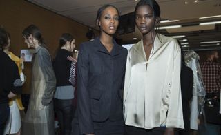 two female models stood in a room with people in the background