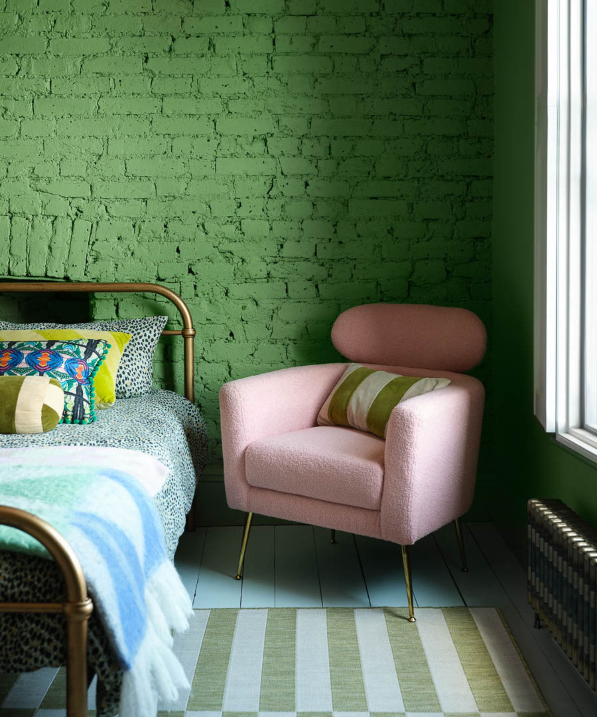 Green painted brick wall in bedroom with striped rug and pink accent chair