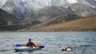 Kate Steels swimming with escort in kayak in New Zealand lake against the backdrop of a snowy mountain