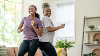 Two women dancing together in living room, smiling