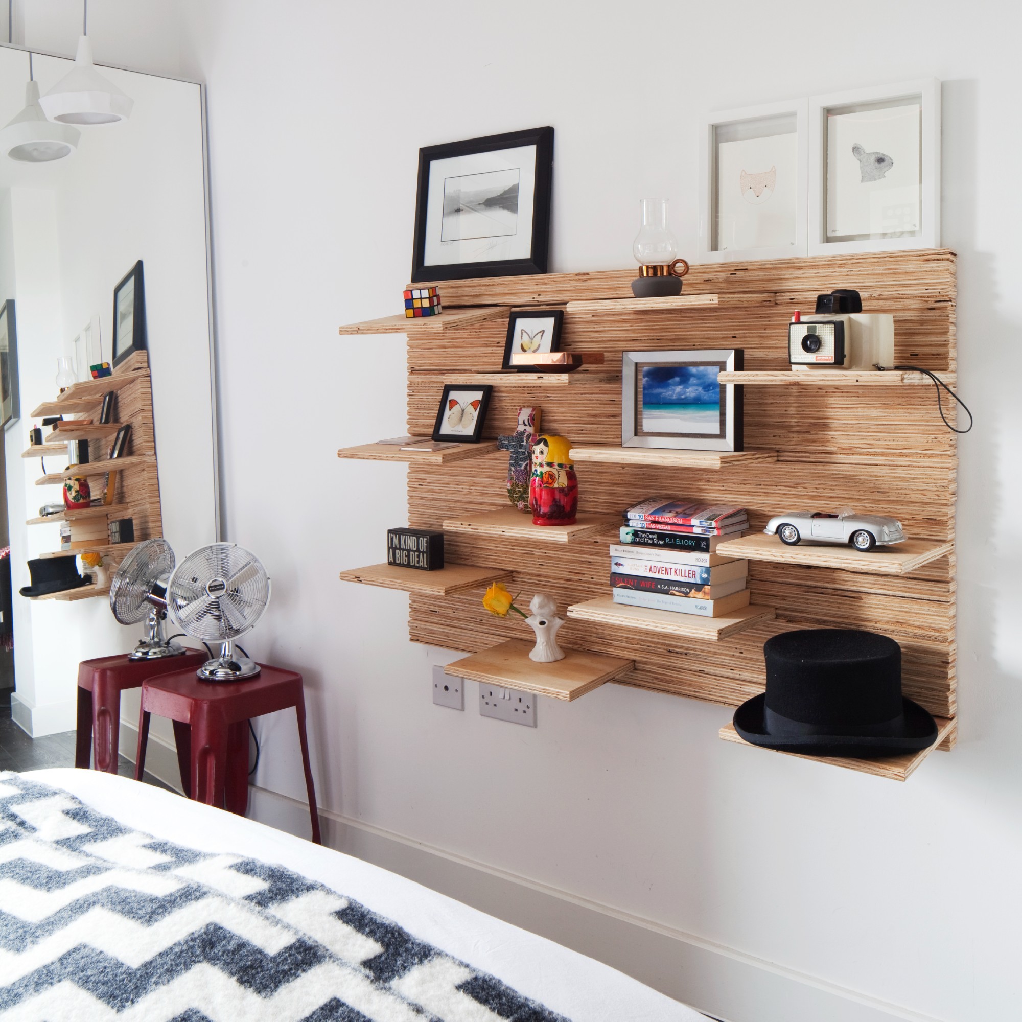A bedroom with a full-length mirror and a shelf display of memorabilia, books and pictures