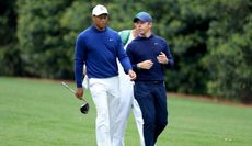 Tiger Woods and Rory McIlroy walk down the fairway whilst chatting 