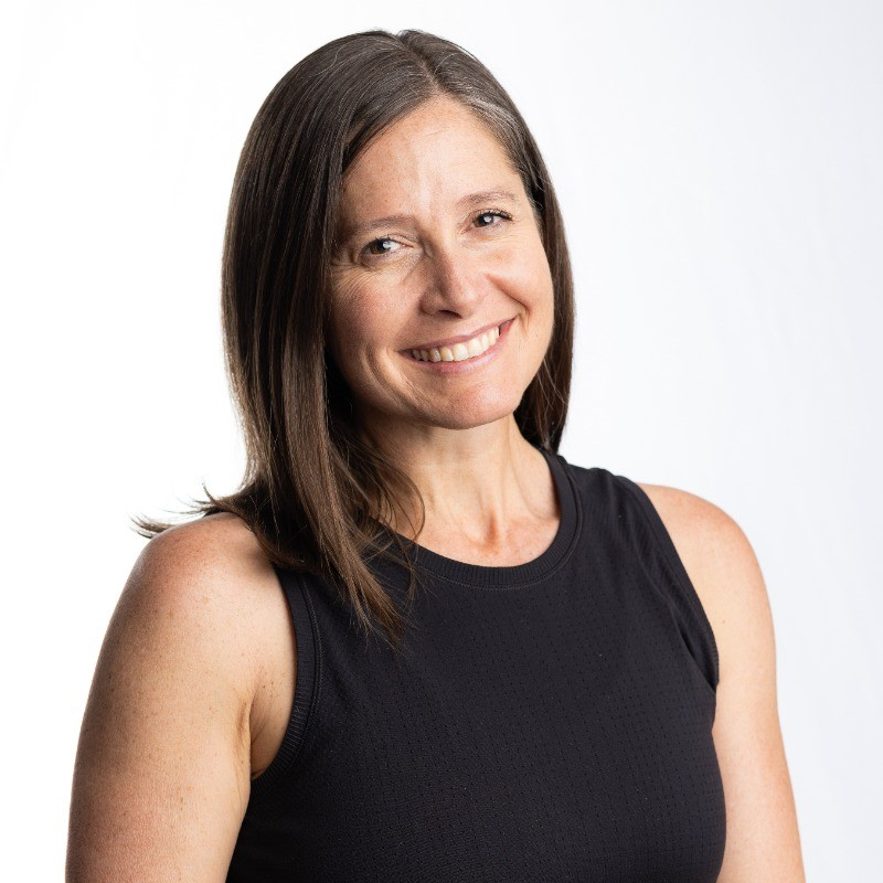 Head and shoulders of woman smiling at the camera. She wears a black tank top.