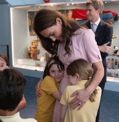Princess Kate wearing a pink dress hugging school children