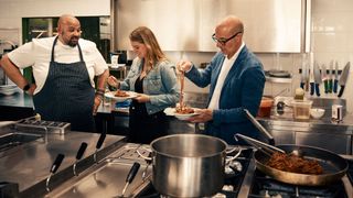 A group of people (Stanley Tucci, right) try pasta in a commercial kitchen, in 'Stanley Tucci: Searching for Italy.'