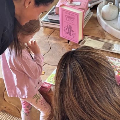 Meghan Markle, Princess Lilibet in a pink outfit and the back of Serena Williams's head in front of a wood coffee table playing Candy Land