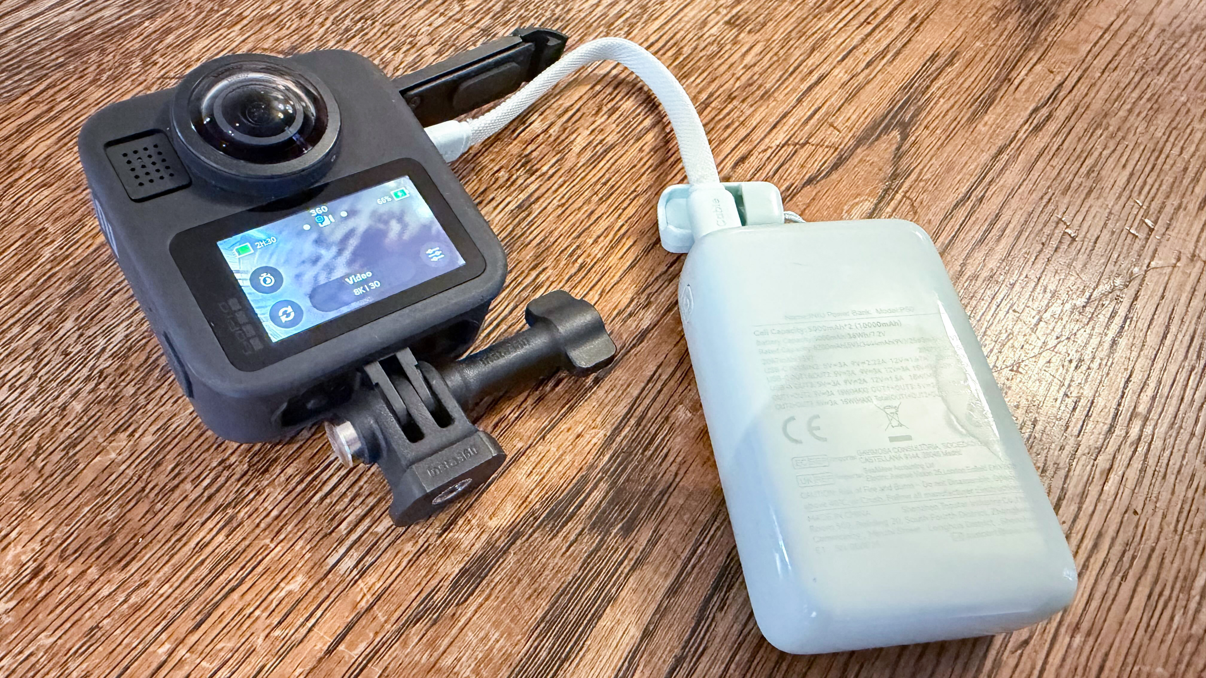 A sage green Iniu Mini Power Bank charging a GoPro MAX2 on a wodden surface.