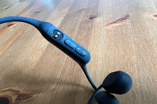 This image shows the Haylou PurFree headphones magnetic charging point close up as well as the operational buttons with a wooden table in the background