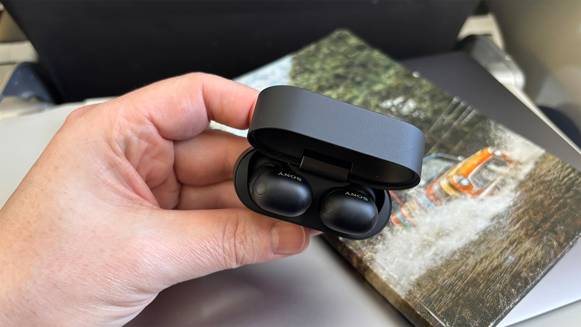 Sony WF-1000XM6 wireless earbuds in open case held in hand next to picture of Mini