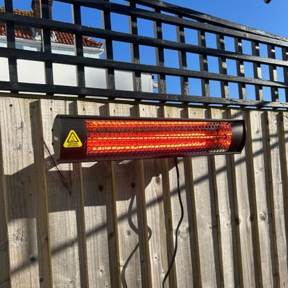 Gtech HeatWave Patio Heater on wooden fence in garden, powered on