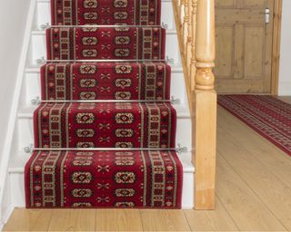 Traditional print carpet stair runner with metal stair rods on wooden staircase