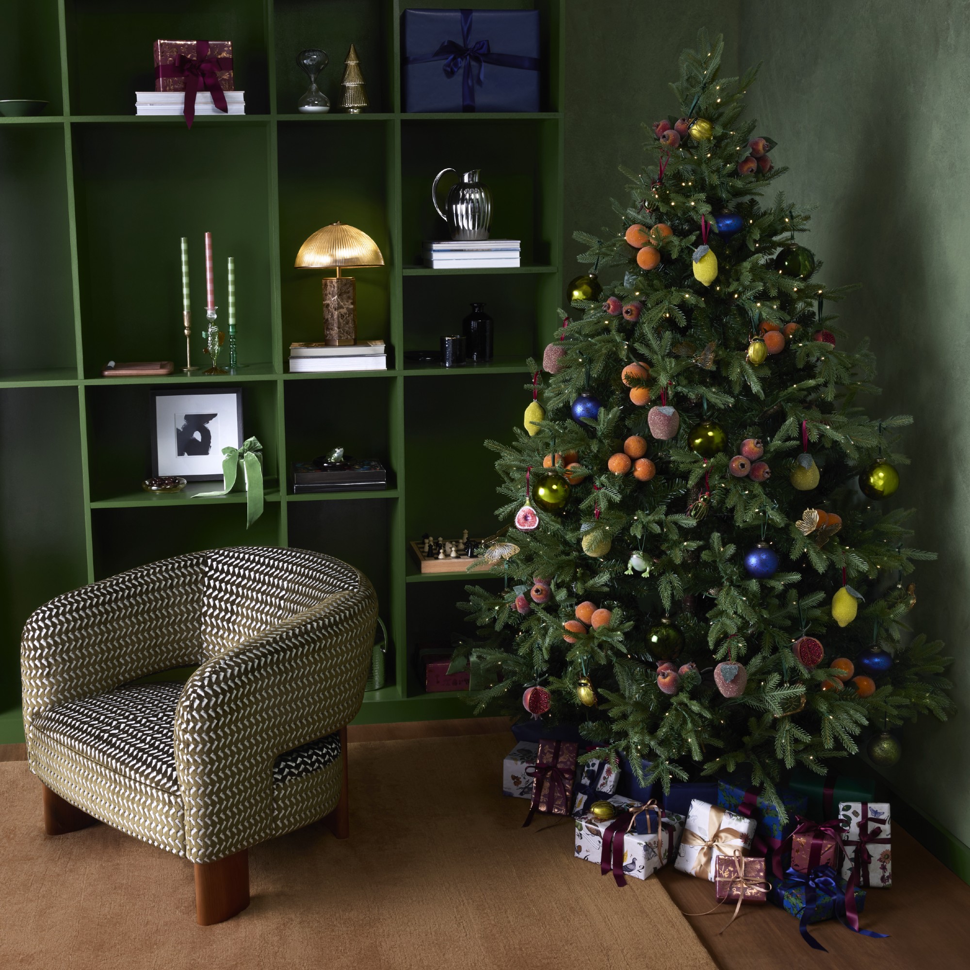A green-painted room with a matching bookshelf decorated for Christmas with a Christmas tree adorned with sugared fruit decorations